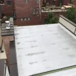 High-angle view of a white, flat commercial roof with a metal-capped chimney.