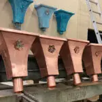 New and weathered copper gutter conductor heads with decorative floral emblems.
