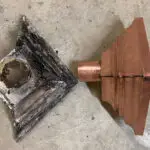Old, corroded metal gutter component next to a new copper replacement.