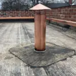 Copper vent pipe with a conical cap on a flat roof.