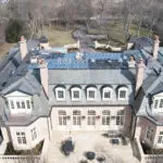 Aerial view of a large stone mansion with an active roof renovation project.