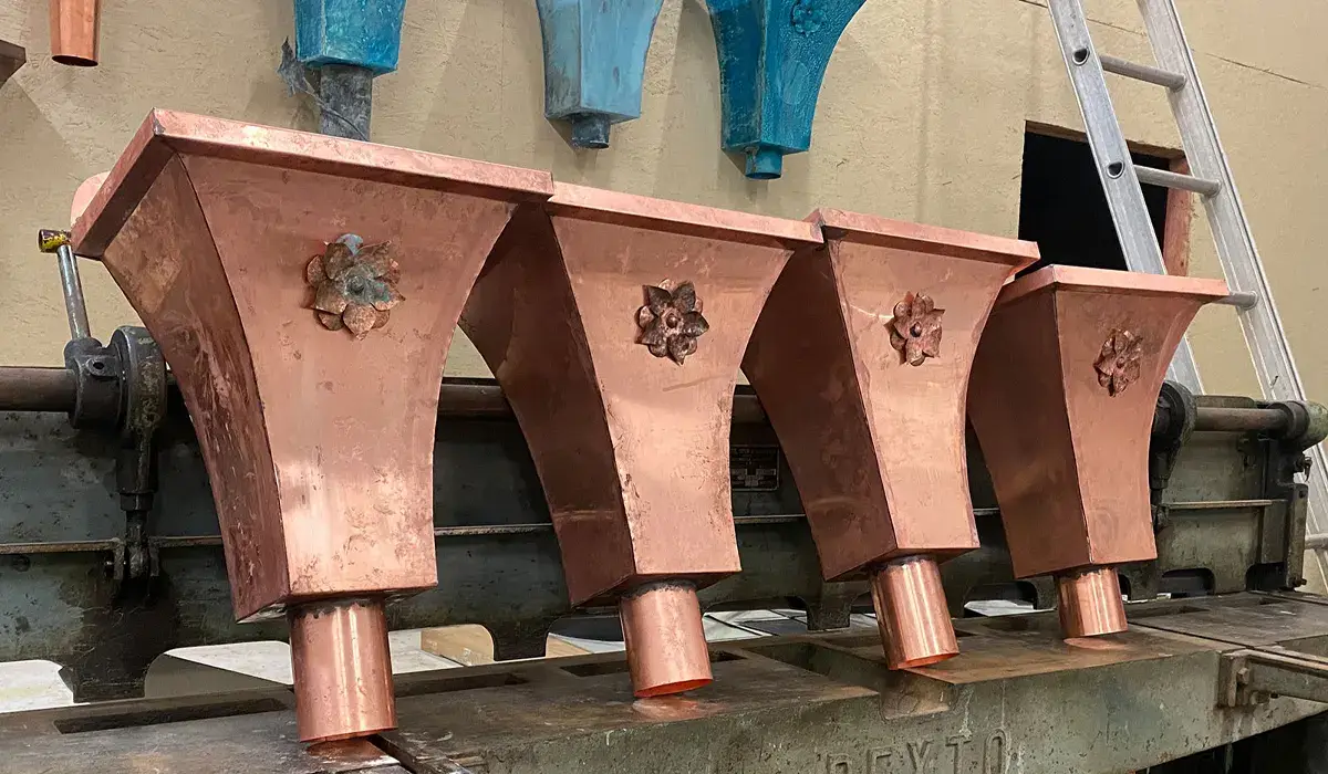 Newly fabricated copper collector boxes beside older green-patinated ones, showing how copper ages