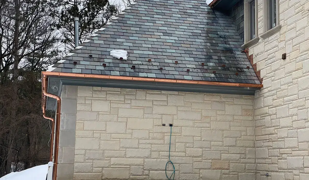 Snow-covered slate roof and copper gutter at the eave, where meltwater refreezes into an ice dam