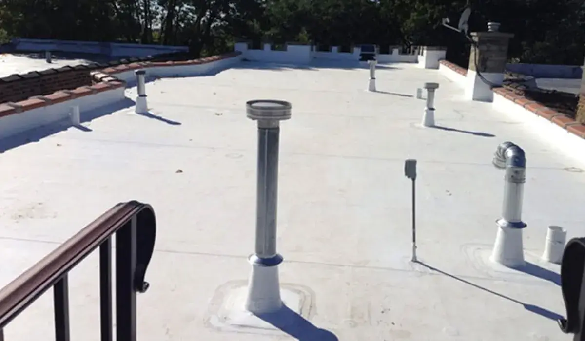 White single-ply membrane roof with pipe penetrations and a guardrail on a low-slope commercial building