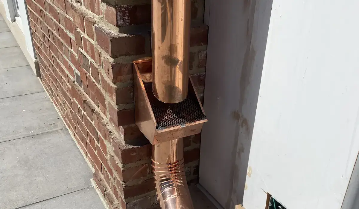 Copper downspout and gutter at a brick wall — soft metal is where hail damage shows first